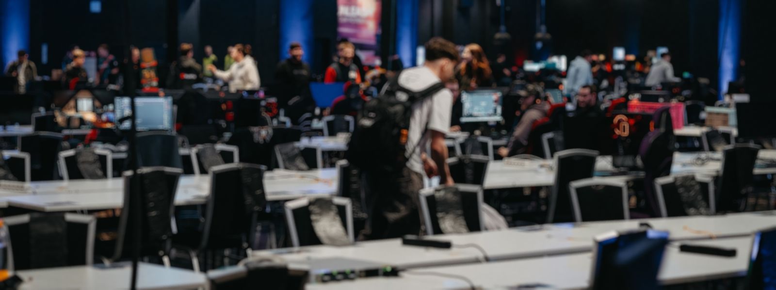 Weite Aufnahme einer LAN-Halle mit langen Tischreihen, Monitoren und Besucherinnen und Besuchern